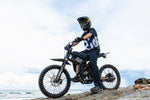 Rider on GT73 Pro electric motorbike with off-road tires on rocky terrain by the sea.
