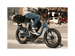 A man riding a blue electric bicycle with an orange Rad Power Bikes logo, fat black tires, and large basket with a cargo net, on a paved road in an urban setting. 
