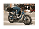 A man riding a blue electric bicycle with an orange Rad Power Bikes logo, fat black tires, and large basket with a cargo net, on a paved road in an urban setting. 