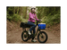 A woman on a trail in a forest sitting on a green cargo ebike with a small front basket and large rear basket wearing a pink jacket and white helmet.